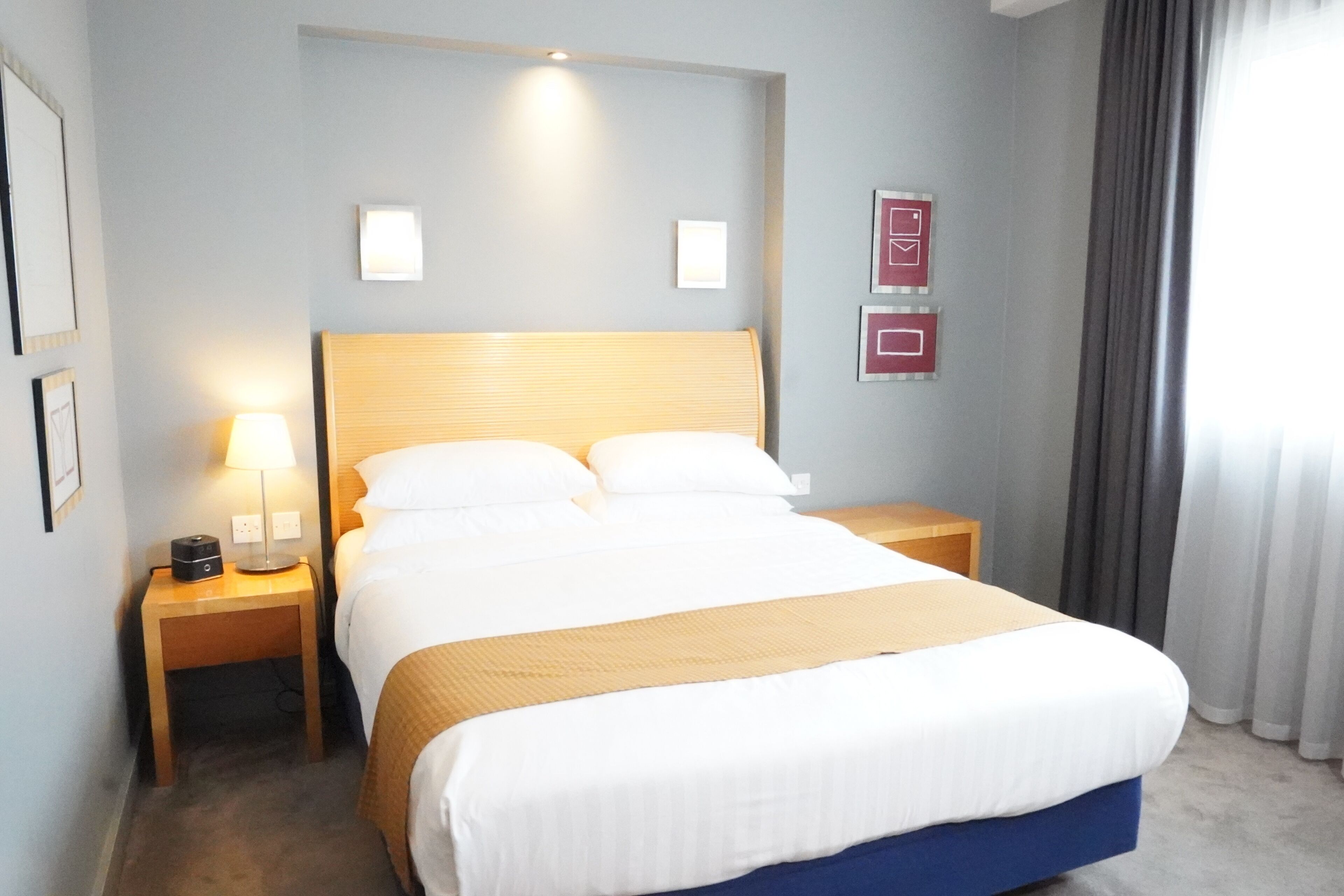 Une chambre d’hôtel avec un grand lit, deux tables de chevet, une lampe et un luminaire fixé au mur.