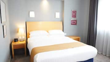 Quarto de hotel com uma cama grande, duas mesas de cabeceira, uma luminária e um ponto de luz na parede.