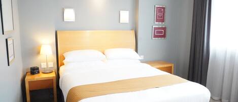 Une chambre d’hôtel avec un grand lit, deux tables de chevet, une lampe et un luminaire fixé au mur.