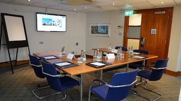 Ett konferensrum med ett långt bord, blå stolar, en projektorduk och en dörr med en utrymningsskylt.