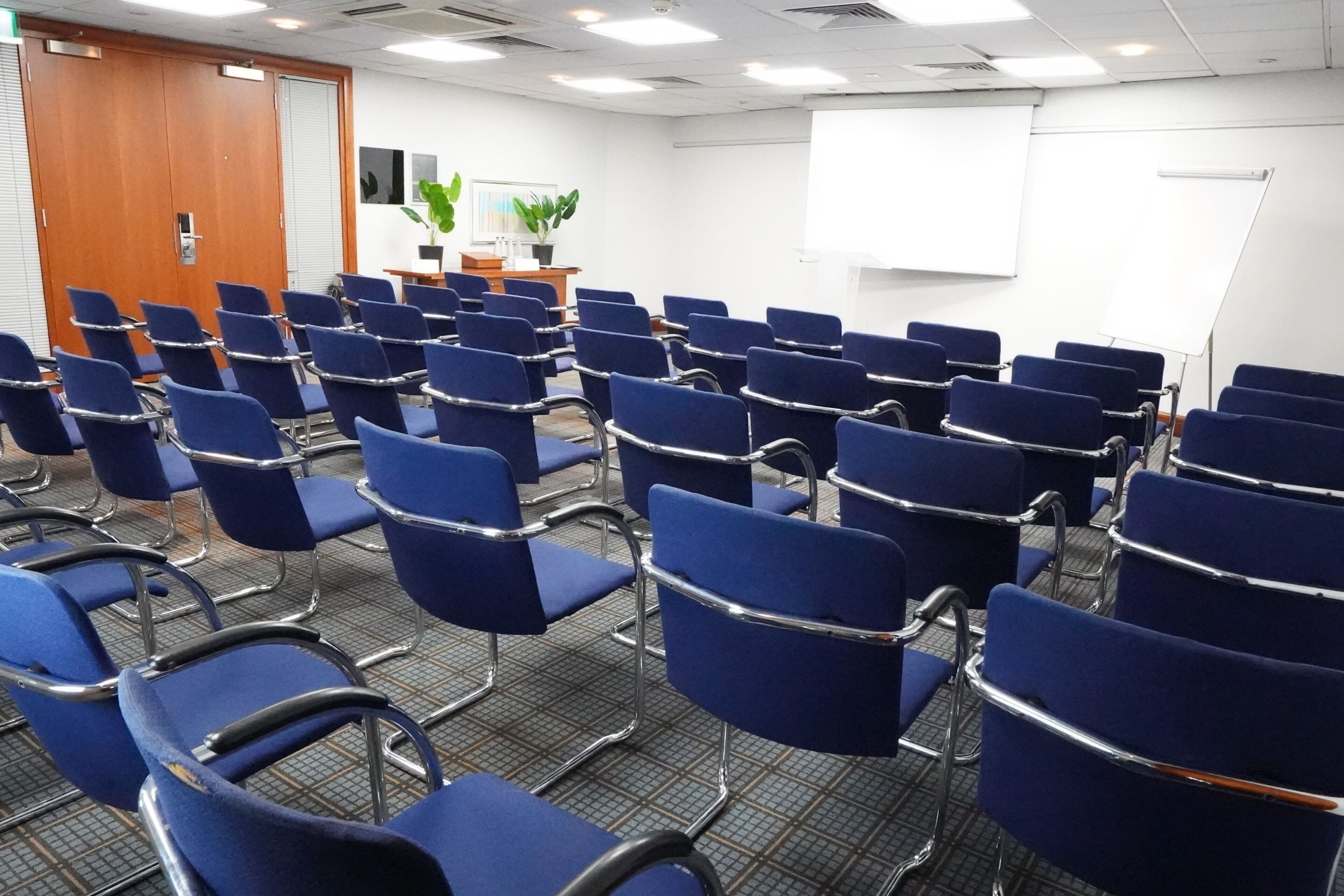 A conference room with rows of blue chairs, a whiteboard, and a wooden door.