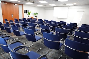 Un salón de conferencias con filas de sillas azules, una pizarra y una puerta de madera.