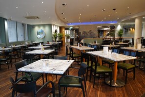 A restaurant interior with multiple dining tables and chairs, a staircase, and a view of the street outside. - Best Western Heathrow Ariel T2, 3, 4 (Hayes)
