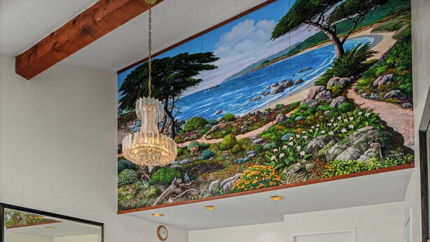 A bathroom with a large mural of a coastal landscape, a hanging chandelier, a mirror, and a tiled floor. - Scottish Fairway Inn (Monterey)