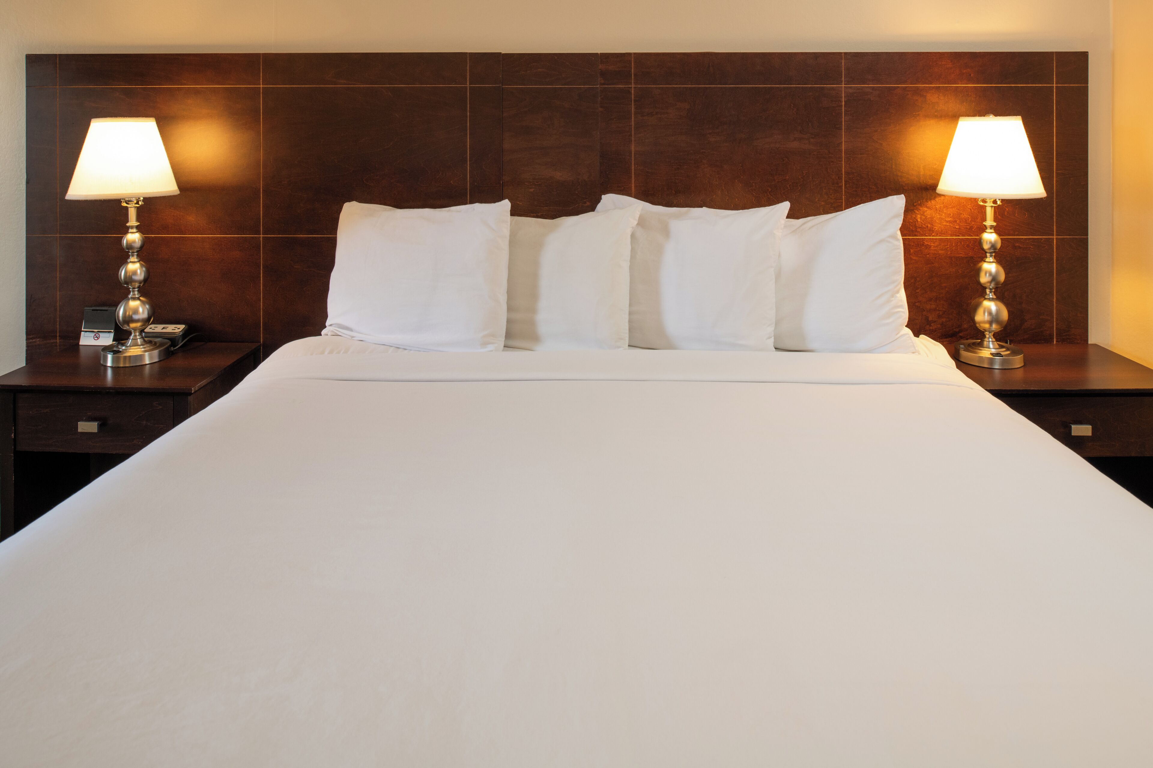 Quarto de hotel com uma cama grande, duas mesas de cabeceira com abajures e uma cabeceira de madeira.