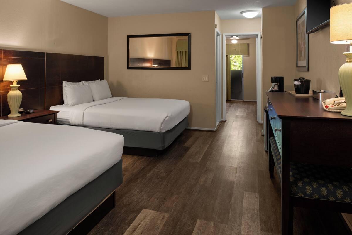 A hotel room with two beds, a desk, a lamp, a mirror, and a door leading to a hallway.