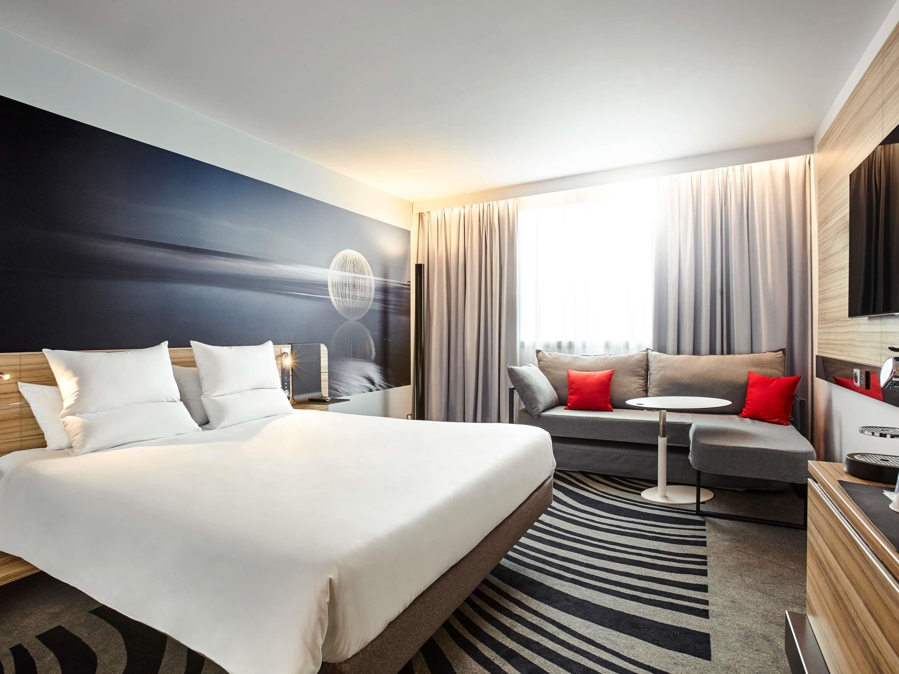 A modern hotel room with a large bed, a sofa, a small table, and a TV.
