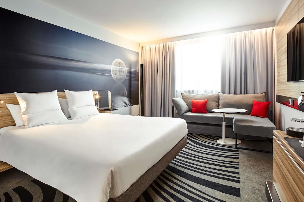 A modern hotel room with a large bed, a sofa, a small table, and a TV.