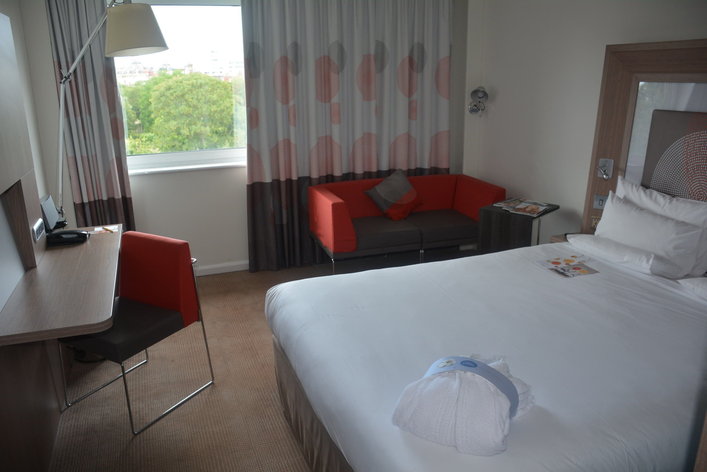 A hotel room with a bed, a desk, a chair, a small table, and a window with curtains.