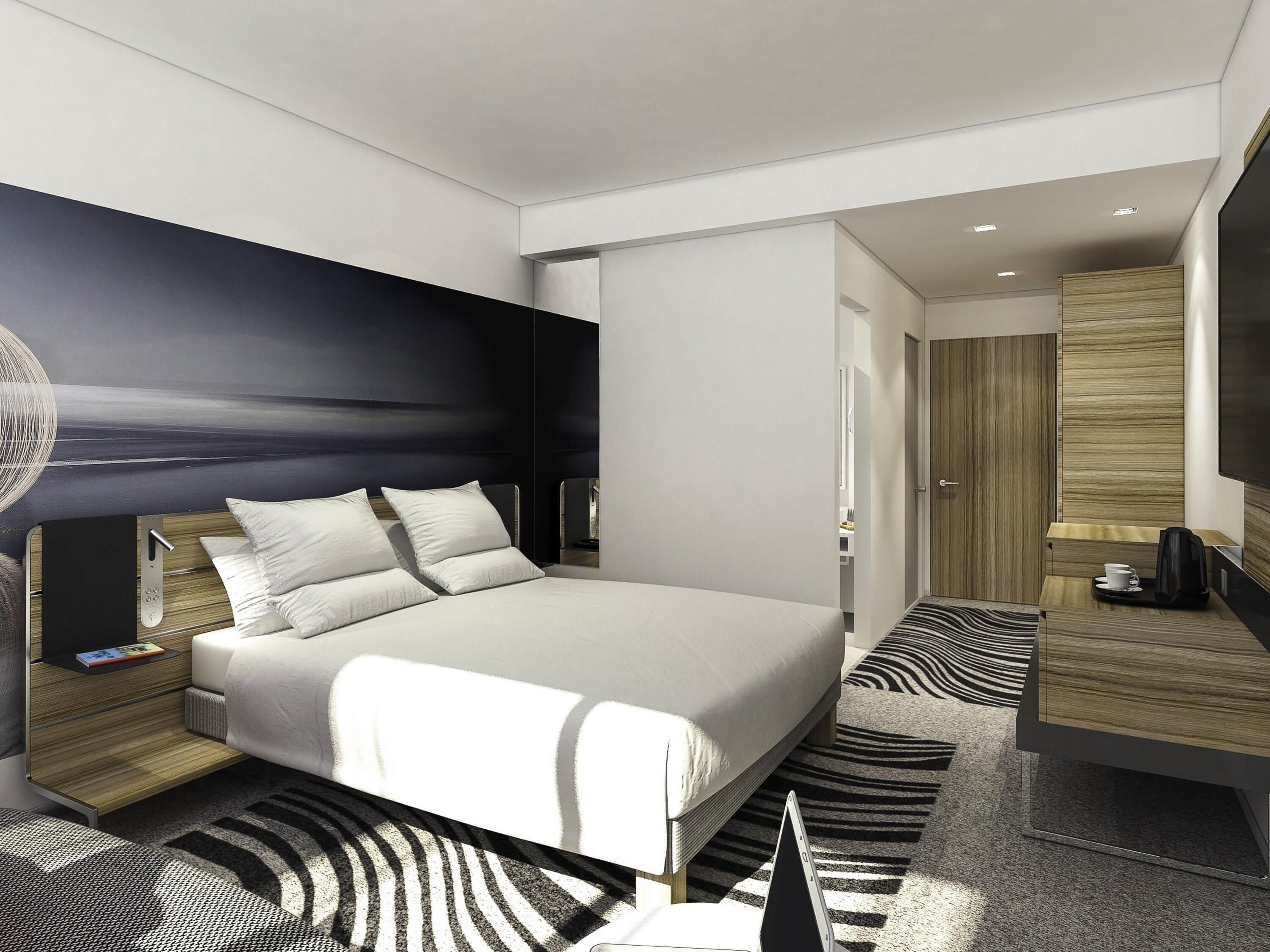 A modern hotel room with a large bed, bedside tables, a desk, and a television.