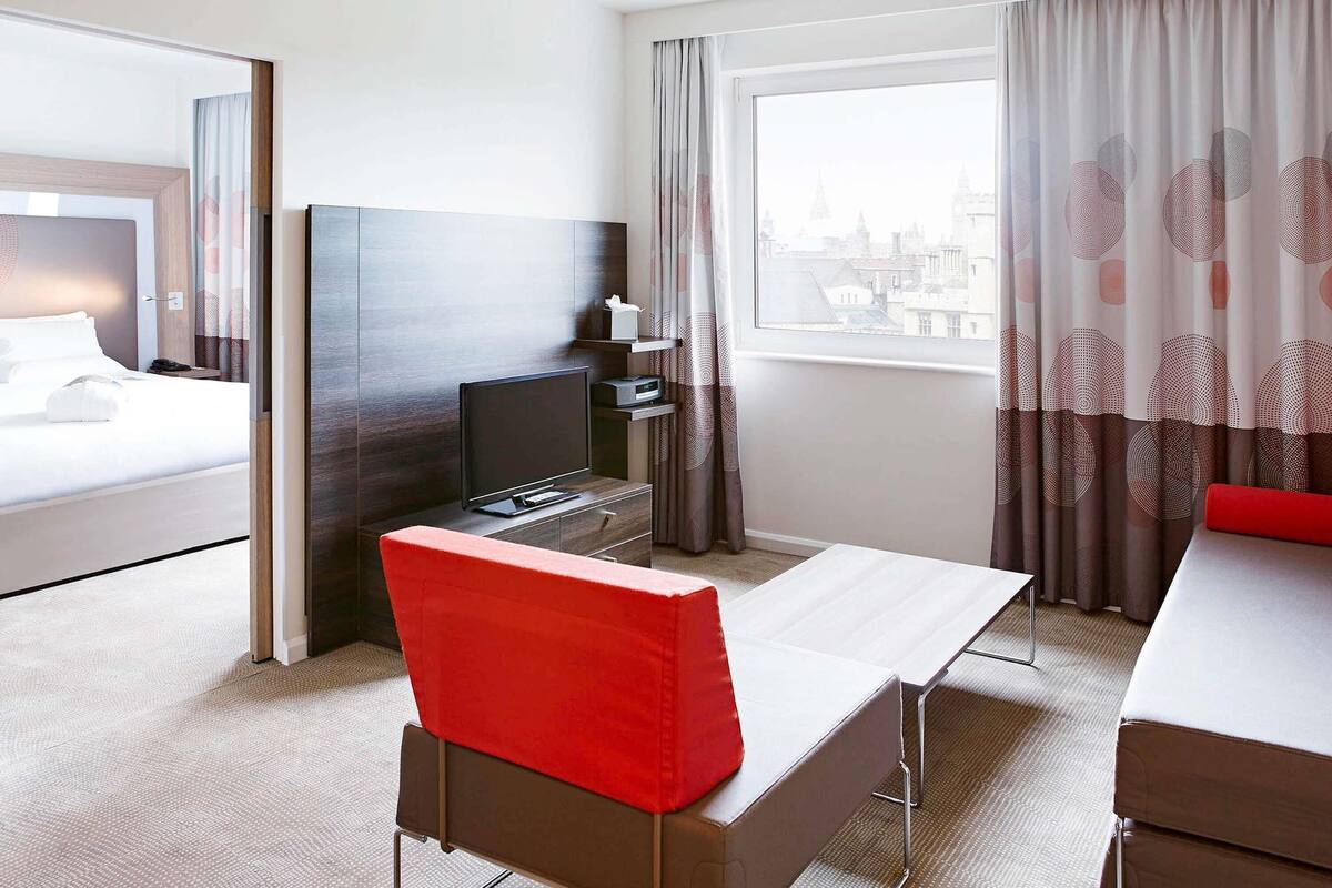 A hotel room with a bed, a desk, a TV, and a window with curtains.