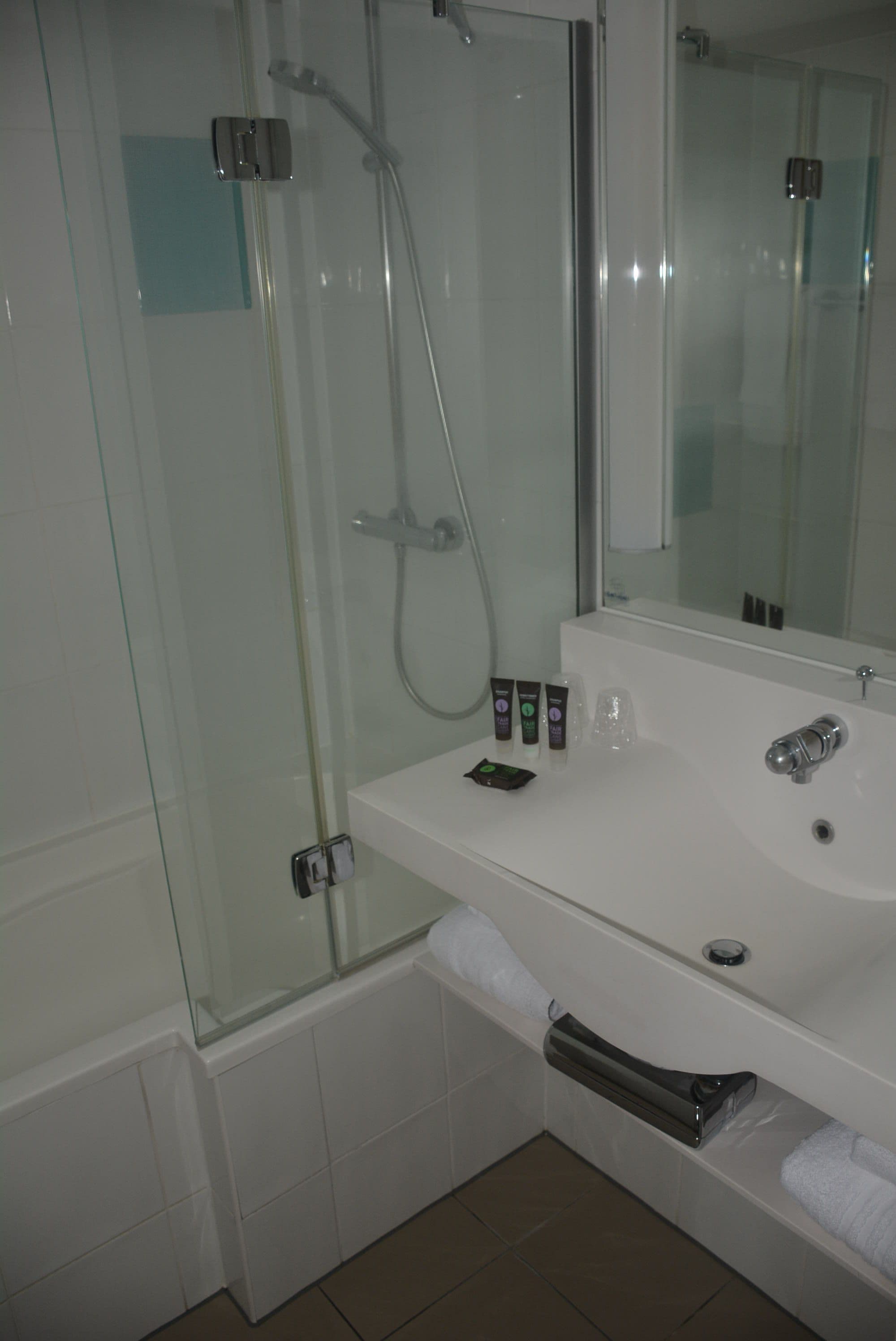 A bathroom with a glass-enclosed shower, a white sink with toiletries, and a mirror above the sink.