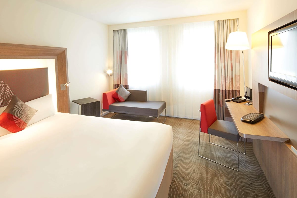 Ett hotellrum med en säng, ett skrivbord med en stol, en soffa och en tv.