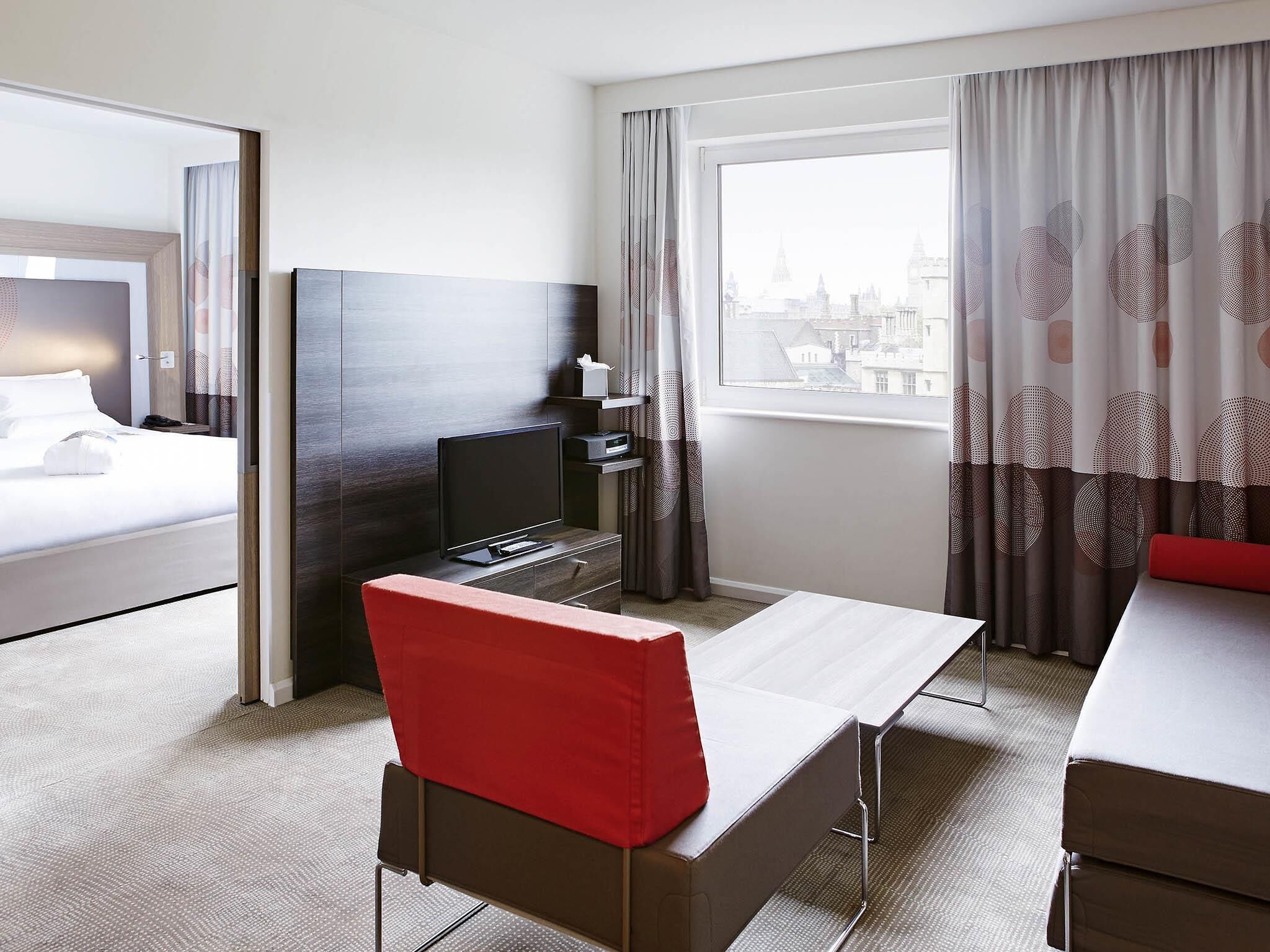 A hotel room with a bed, a TV, a desk with a chair, and a window with curtains.