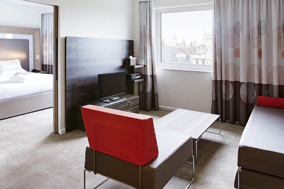 A hotel room with a bed, a TV, a desk with a chair, and a window with curtains.
