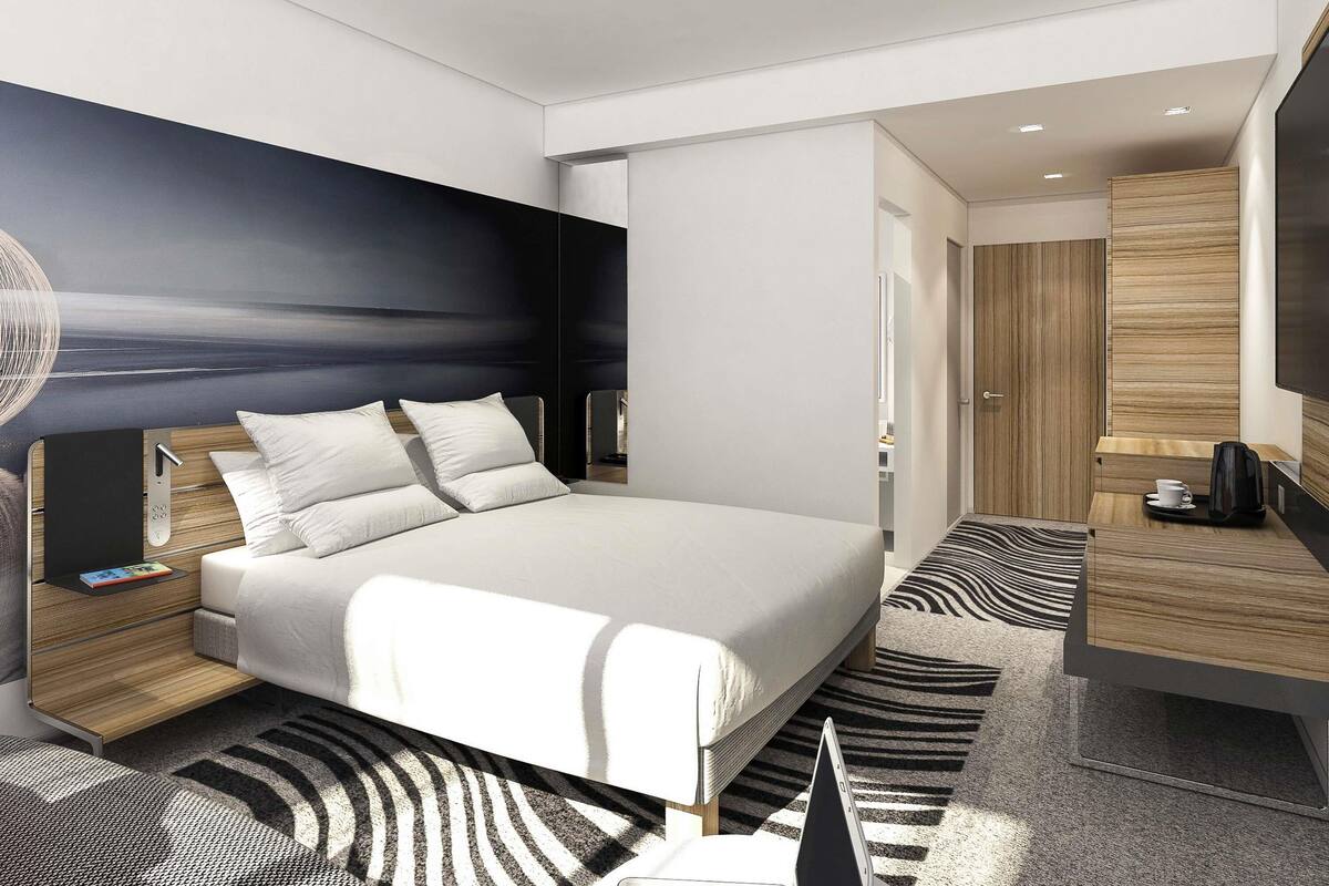 A modern hotel room with a large bed, bedside tables, a desk, and a flat-screen TV.