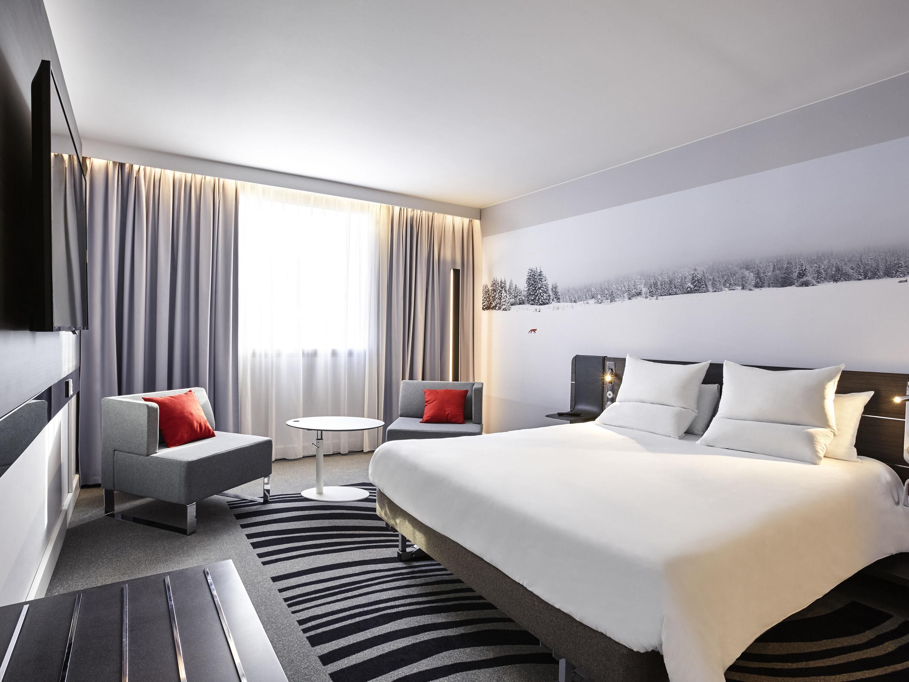 A modern hotel room with a large bed, a sofa, a small round table, and a TV.