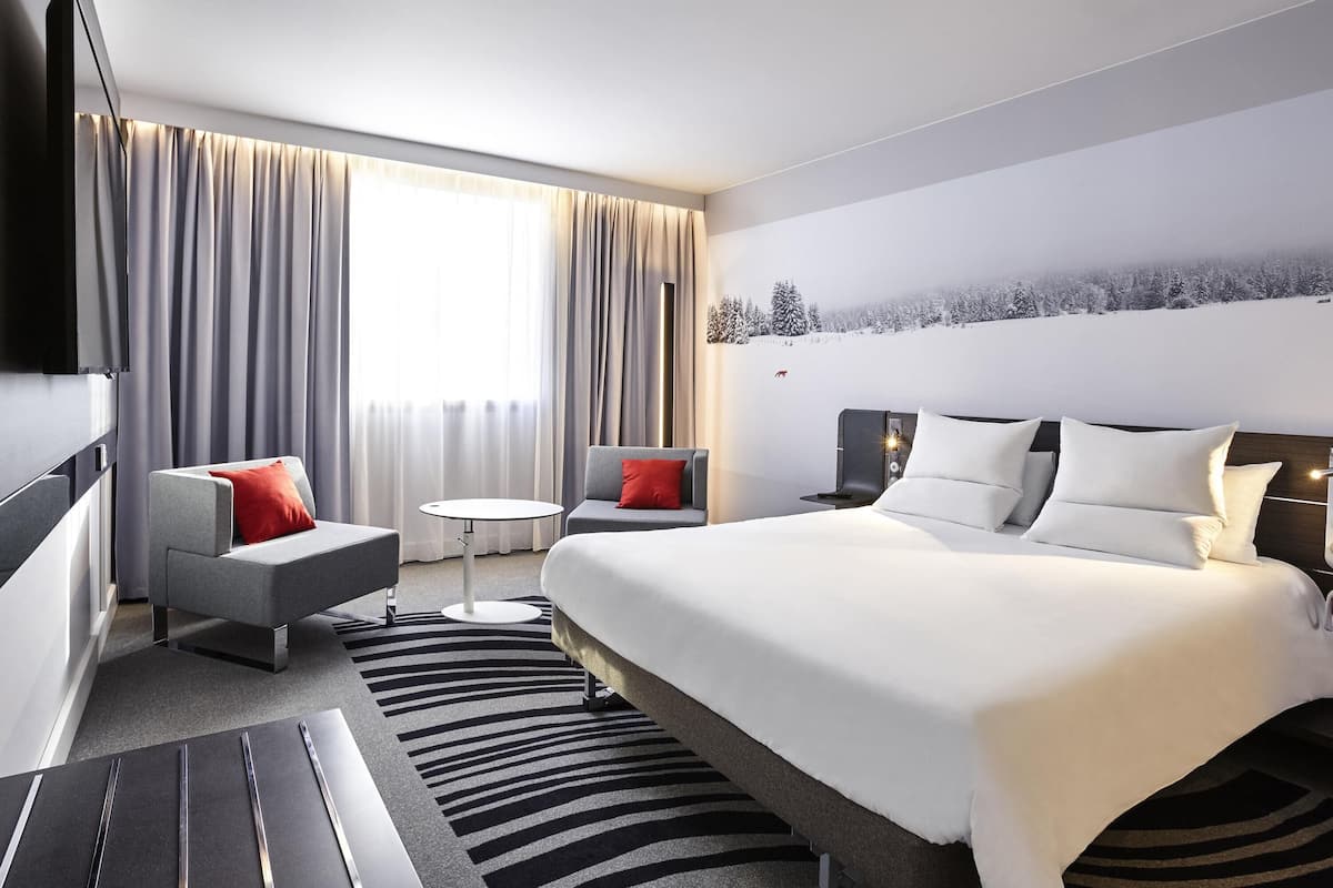A modern hotel room with a large bed, a sofa, a small round table, and a TV.