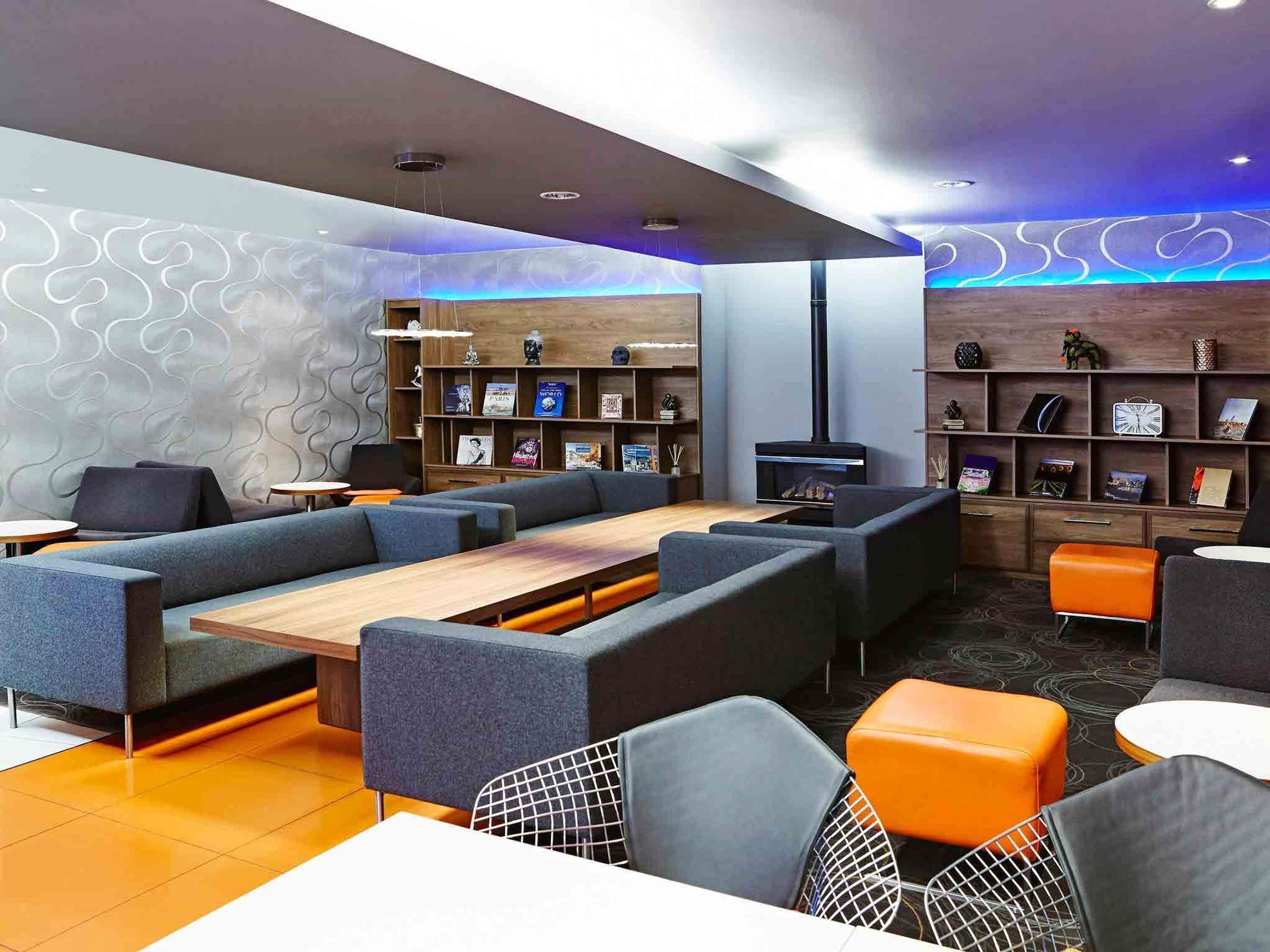 A modern lounge area with sofas, a long table, and a bookshelf.