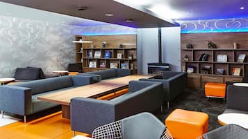 A modern lounge area with sofas, a long table, and a bookshelf.