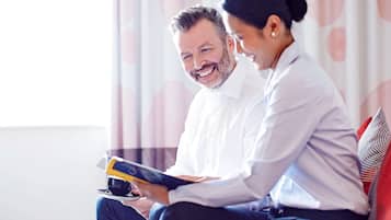 Two people sitting on a couch, one holding a tablet and a cup.
