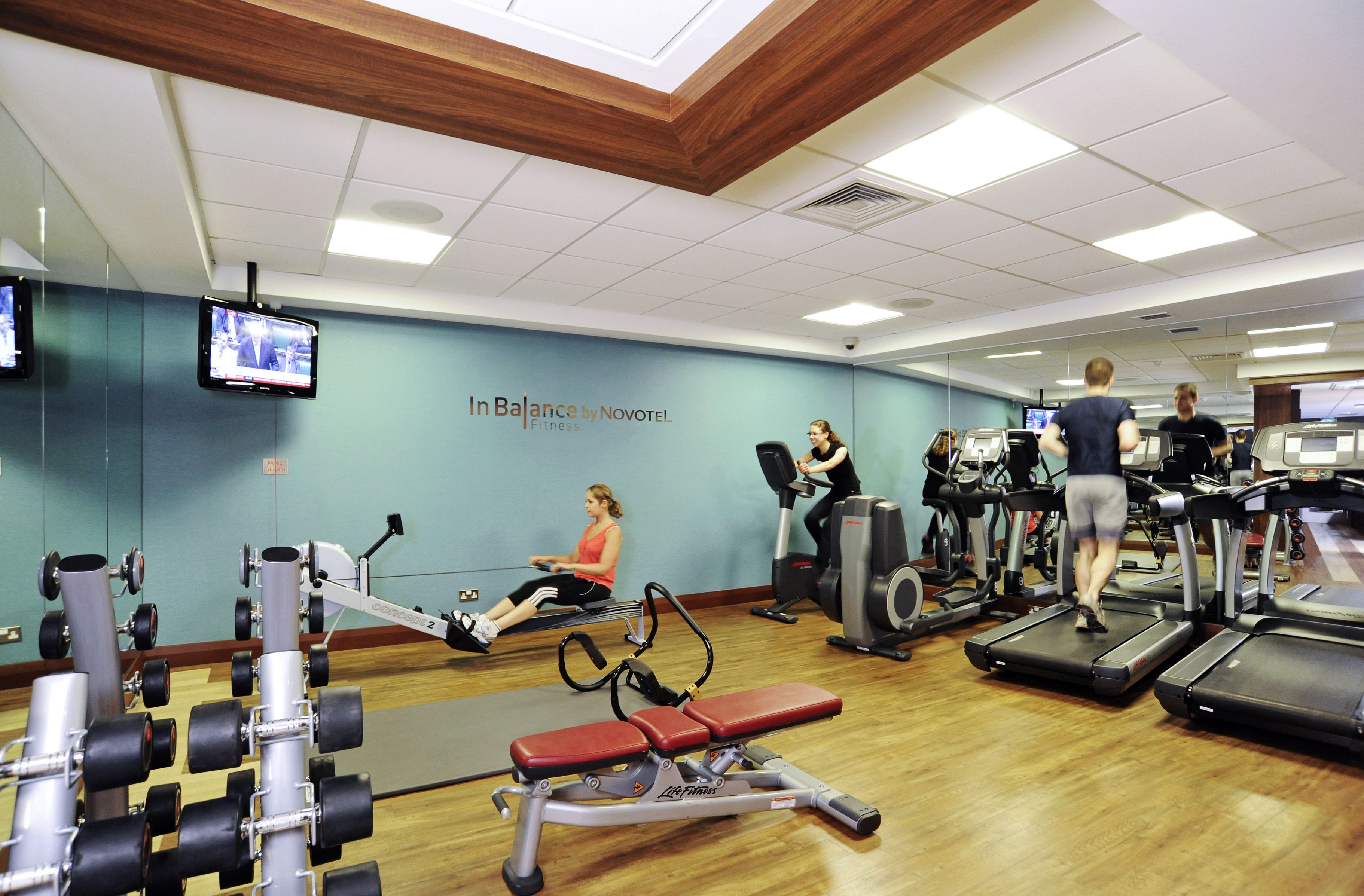 A gym with exercise equipment, a television, and a wall with the text "In Balance by Novotel Fitness".