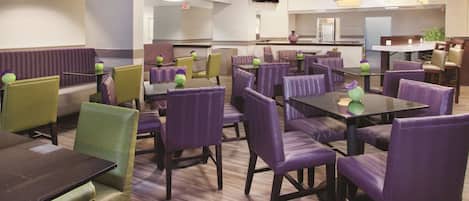 A restaurant with purple and green booths and tables, a flat-screen TV on the wall, and a kitchen area in the background.