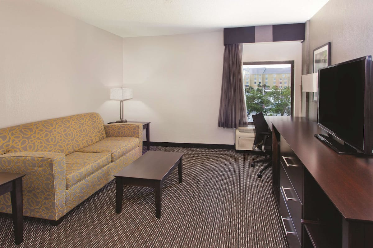 A hotel room with a sofa, a small table, a TV, and a window with curtains.