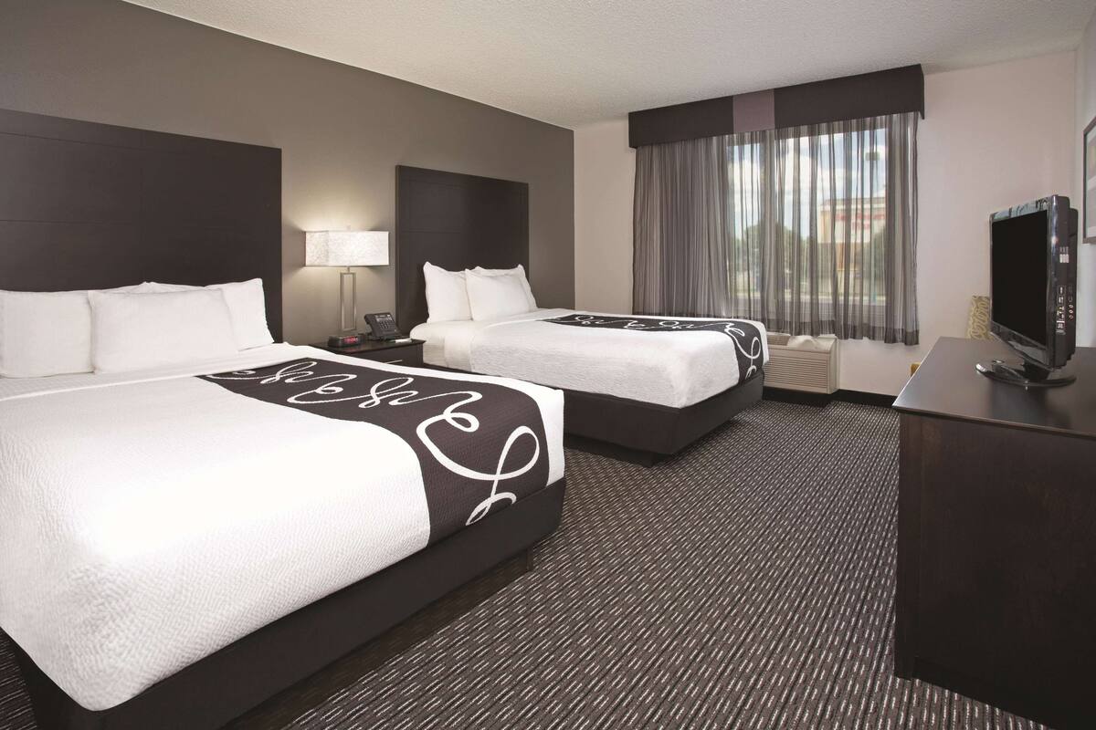 A hotel room with two beds, a desk, a TV, and a window with curtains.