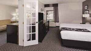 Ein Hotelzimmer mit Bett, Schreibtisch, Kommode, Fernseher und einem fensterbepflanzten Fenster.