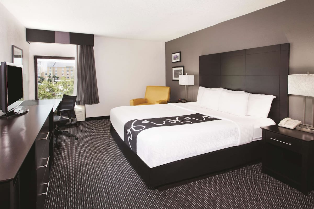 A hotel room with a bed, a desk, a chair, a TV, and a window with curtains.