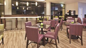 Ein Hotel-Speisebereich mit mehreren Tischen und Stühlen, einer Bar und großen Fenstern.