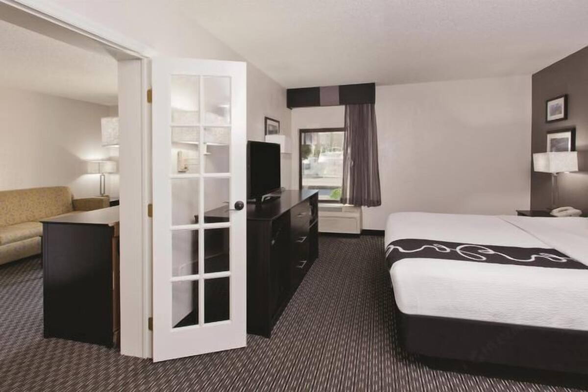 A hotel room with a bed, a desk, a dresser, a TV, and a window with curtains.