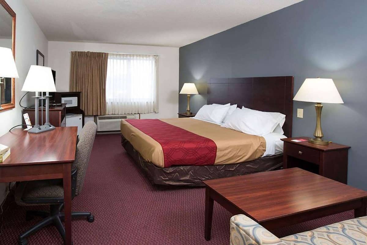A hotel room with a bed, two bedside tables with lamps, a desk with a chair, a small table, and a large mirror.
