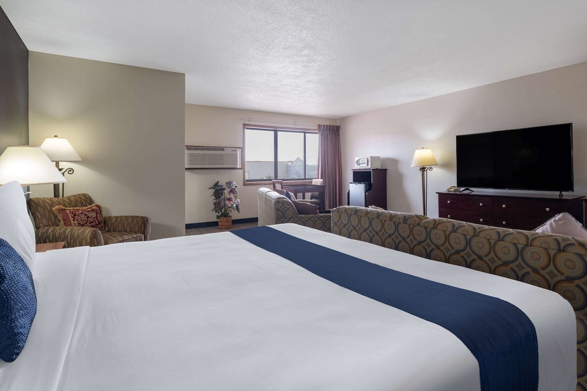 A hotel room with a large bed, two armchairs, a desk with a chair, a television, and a window with curtains.