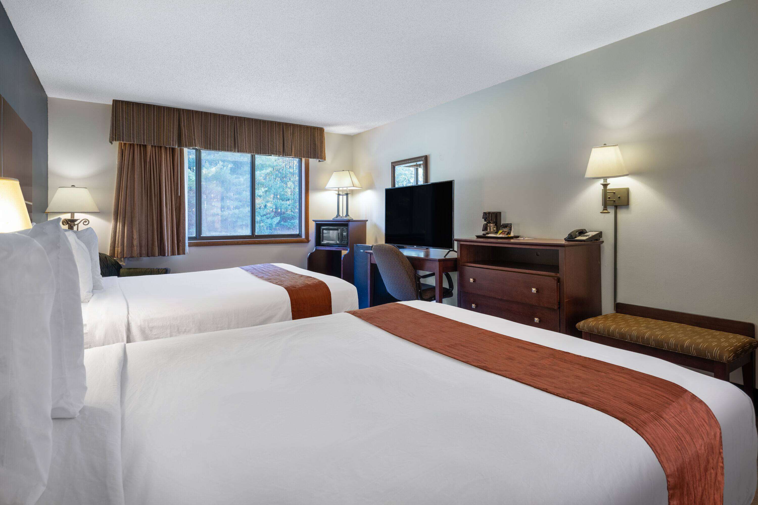 A hotel room with two beds, a desk with a computer, a television, and a window with curtains.