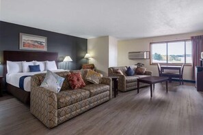 A hotel room with a bed, two sofas, a coffee table, and a large window. - Travelodge by Wyndham Merrill (Merrill)
