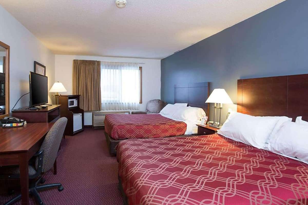 A hotel room with two beds, a desk with a computer, a chair, a TV, and a window with curtains.