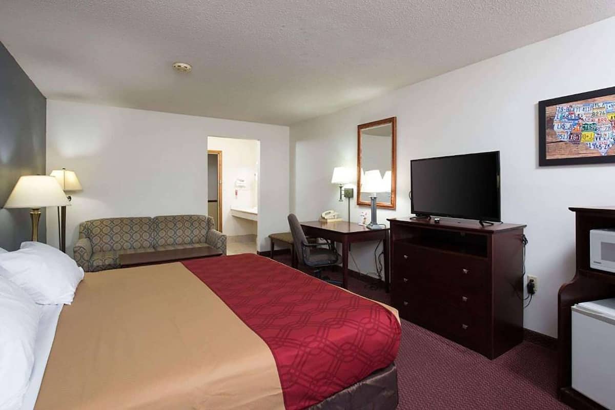 A hotel room with a bed, a desk, a chair, a television, and a small refrigerator.