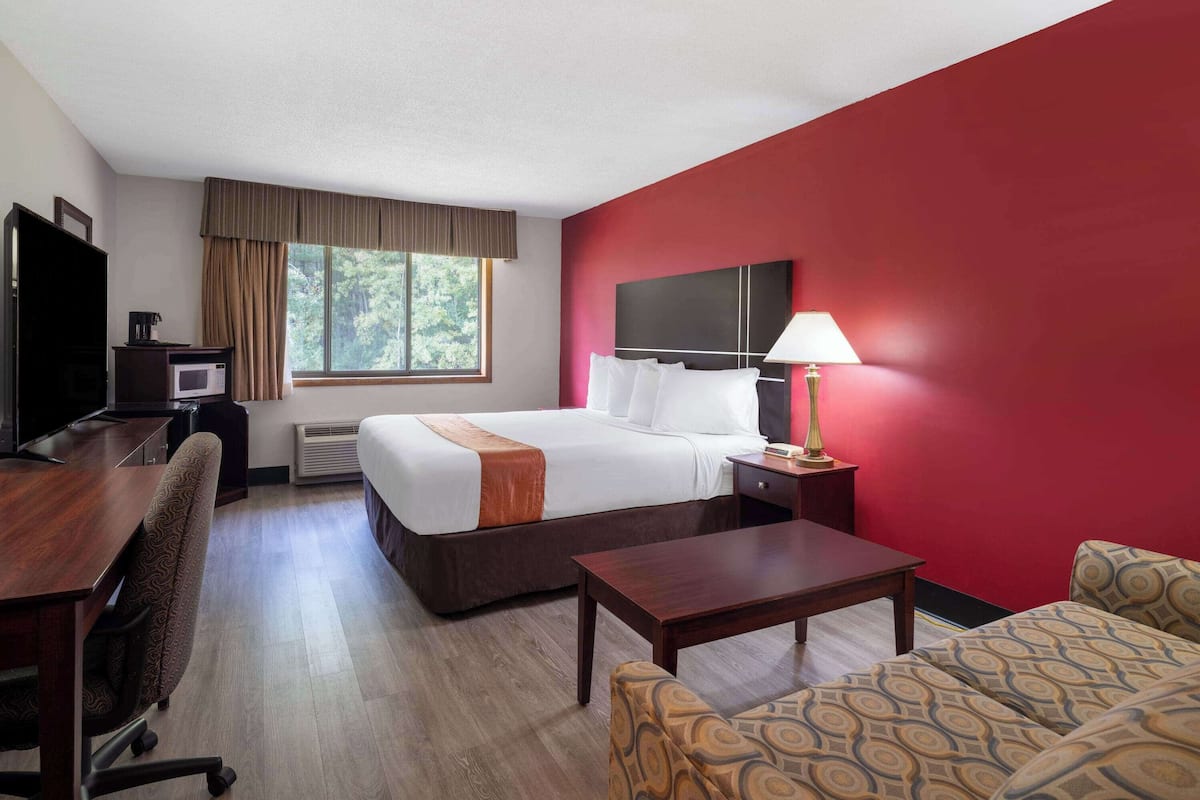 A hotel room with a bed, desk, chair, and a TV.