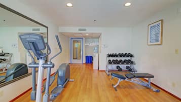 A gym with cardio equipment, dumbbells, and a bench.