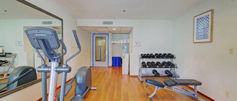 A gym with cardio equipment, dumbbells, and a bench.
