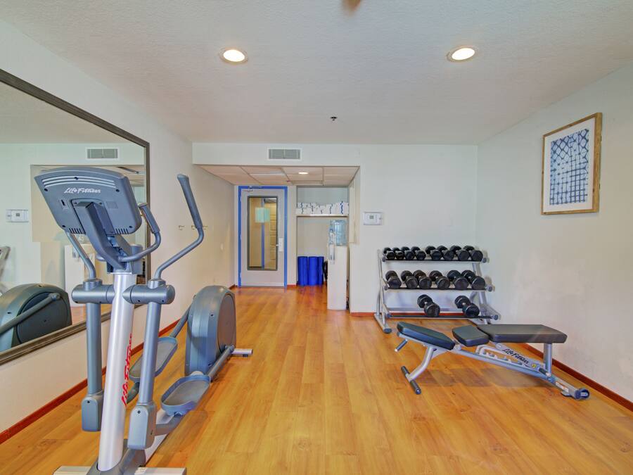 A gym with cardio equipment, dumbbells, and a bench.