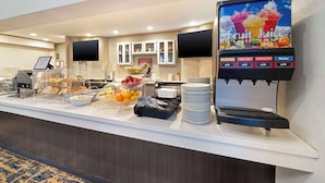 A buffet counter with a fruit juice dispenser, various food items, and a clock on the wall. - Best Western Posada Royale Hotel & Suites (Simi Valley)