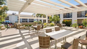 An outdoor patio area with tables and chairs, a pergola, and a view of a building with balconies. - Best Western Posada Royale Hotel & Suites (Simi Valley)