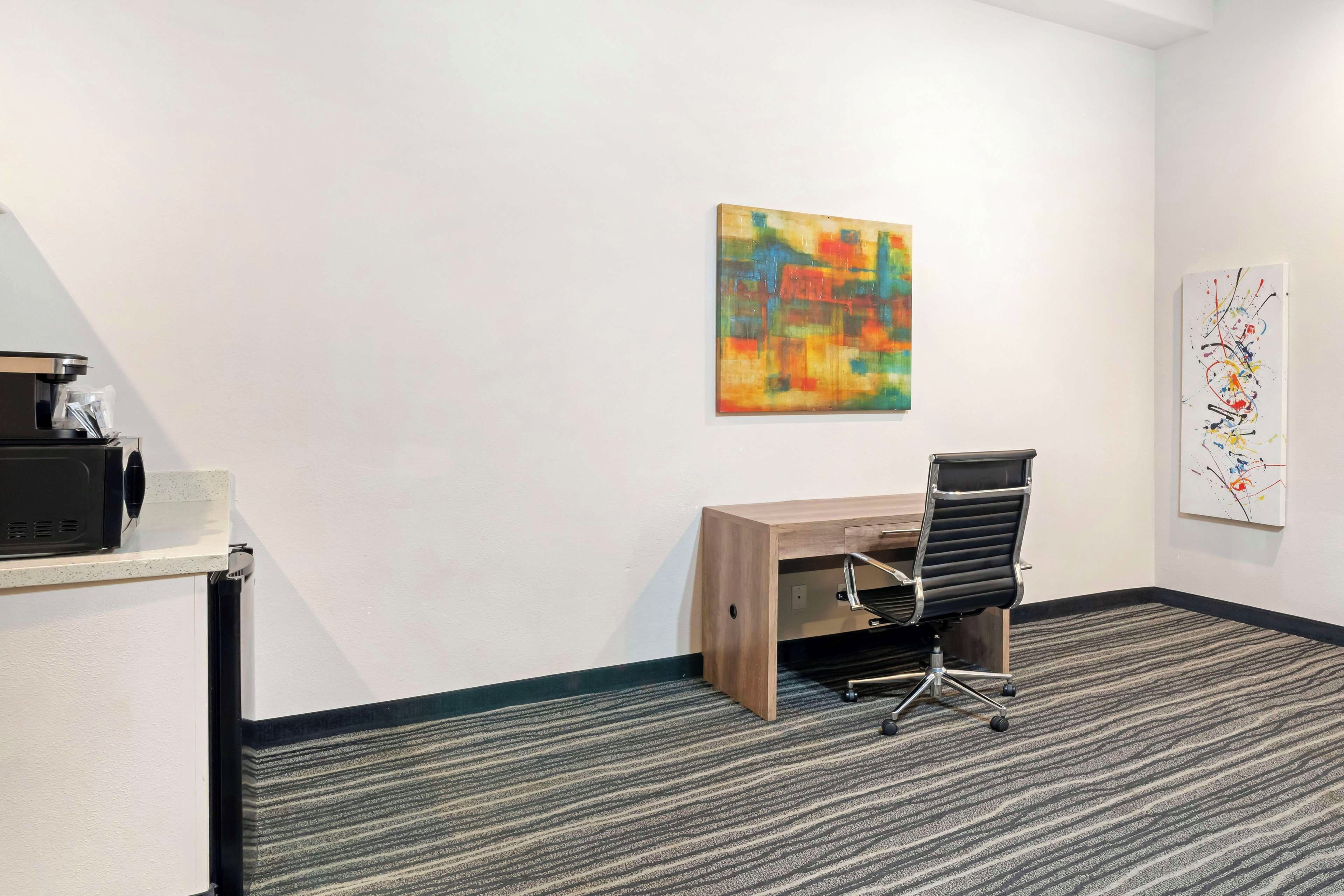 Un pequeño espacio de oficina con un escritorio, una silla y dos obras de arte en las paredes.