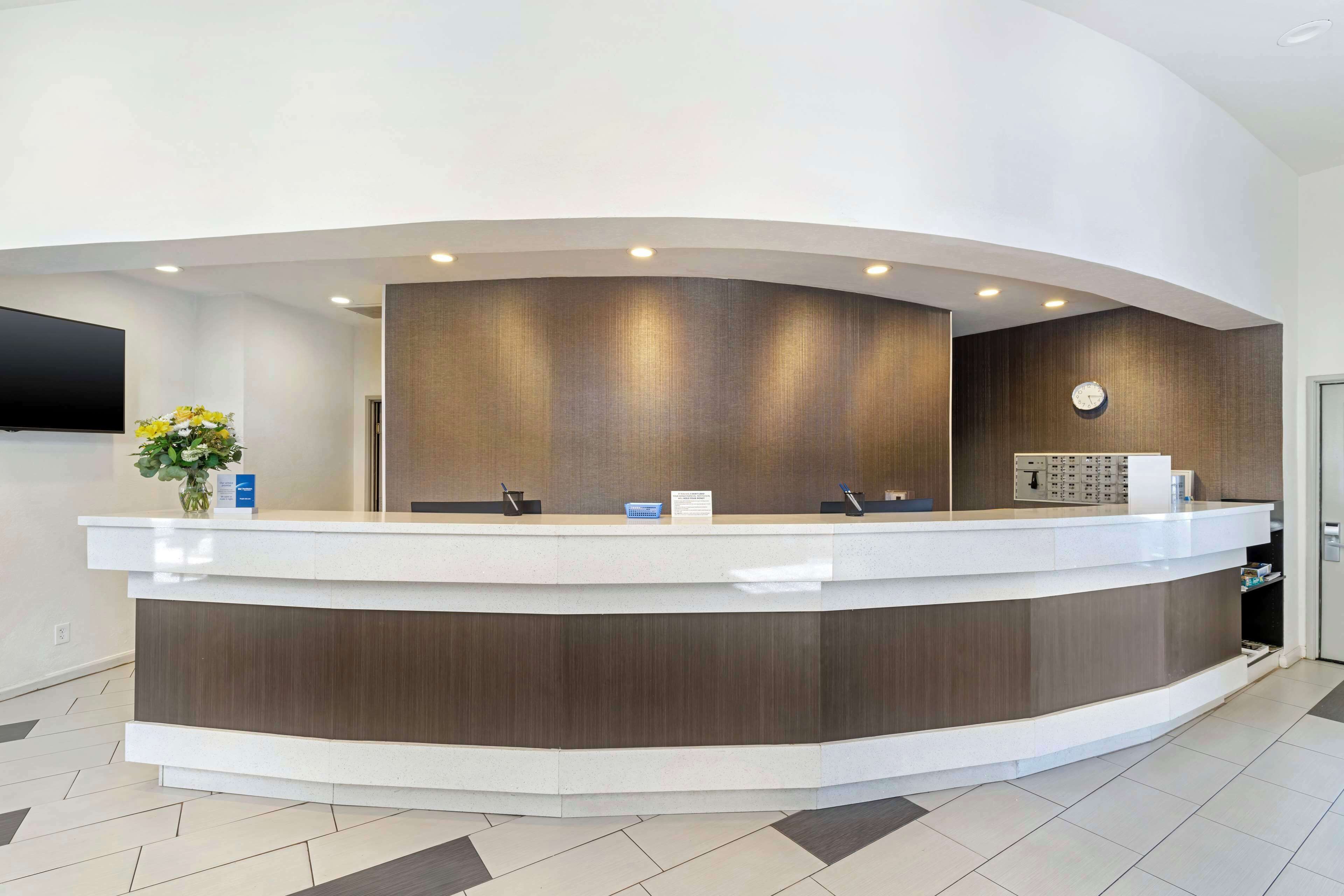 A reception desk with a curved design, a flat-screen TV mounted on the wall, and a clock above the desk.