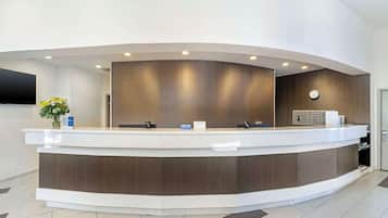 A reception desk with a curved design, a flat-screen TV mounted on the wall, and a clock above the desk.