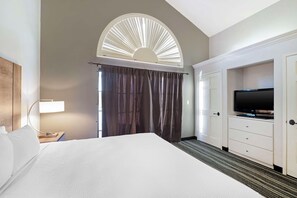 A hotel room with a bed, a TV, a desk with a lamp, and a large window with curtains. - Best Western Posada Royale Hotel & Suites (Simi Valley)