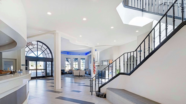 A spacious lobby with a staircase, a reception desk, and large windows allowing natural light. - Best Western Posada Royale Hotel & Suites (Simi Valley)